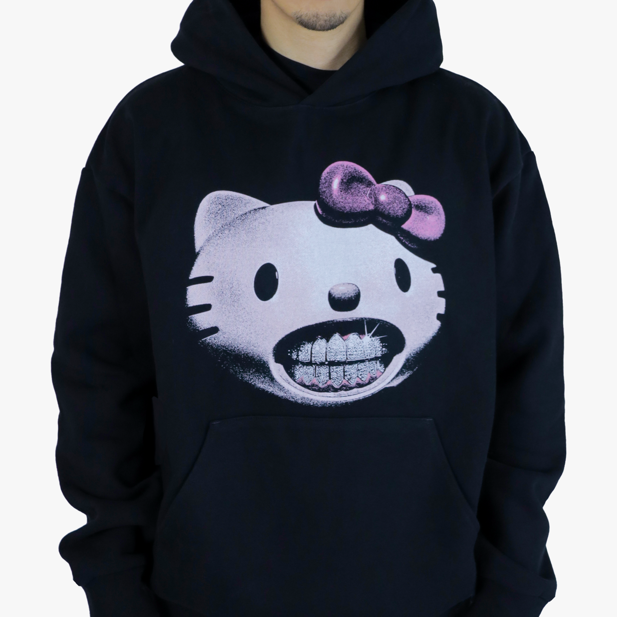 Model wearing a black hoodie featuring a graphic of a light pink cat head with diamond grillz in her teeth and a pink bow on her ear, offering a blend of cute and edgy style. Set on a white background. Available for $79.95 USD 