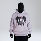 Model wearing a grey hoodie featuring a graphic of a stylized character head with pigtails and a pink skull motif, complete with diamond grillz. Standing against a neutral background