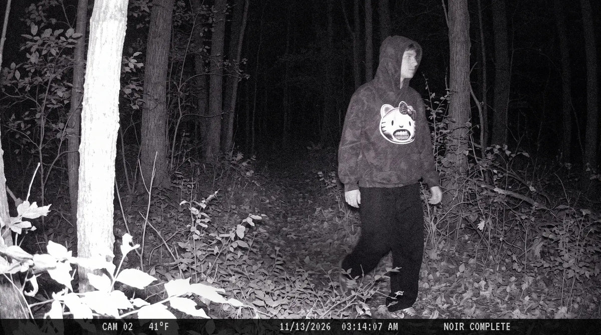 Trail camera night photo of a person in the Icy Kitty camo hoodie walking through the woods, timestamped 11/13/2026