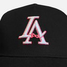 Close up shot of the la bow hat's embroidery, showcasing the white la logo with a pink outline on a black hat.