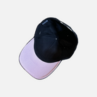 Black hat with a pink color on the underside of the brim. With a woven "Noir Complete" label on the left side of the hat.